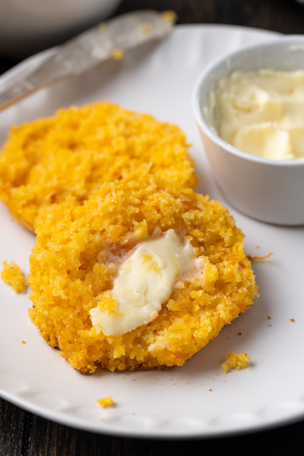 Close up of a sweet potato biscuit cut in half and buttered on a plate, next to a small butter dish.