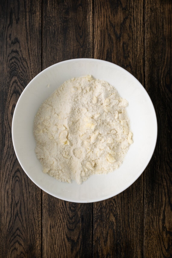 Butter crumbled with flour for biscuit dough in a white mixing bowl.