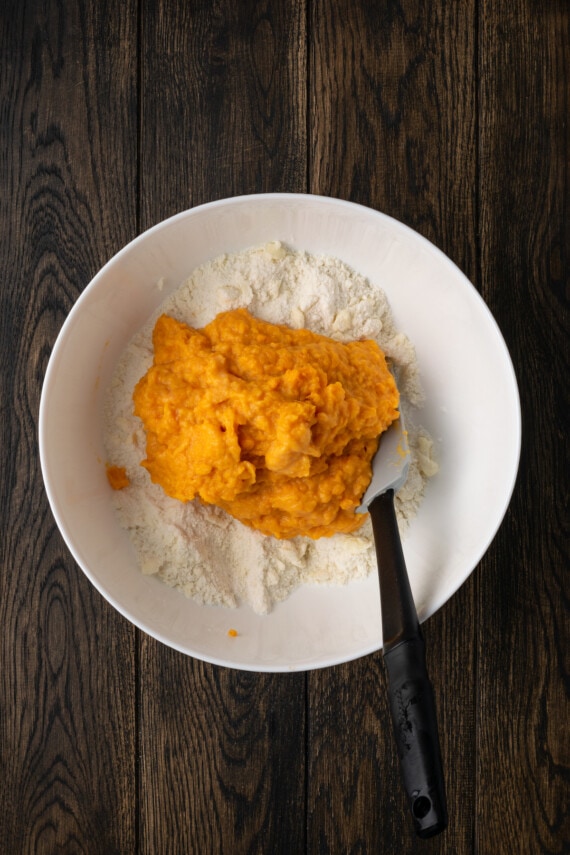 Mashed sweet potato added to biscuit dough ingredients in a white bowl.