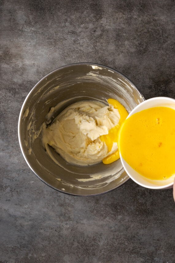 Whisked eggs are added to a mixing bowl with cream cheese, butter, and sugar.