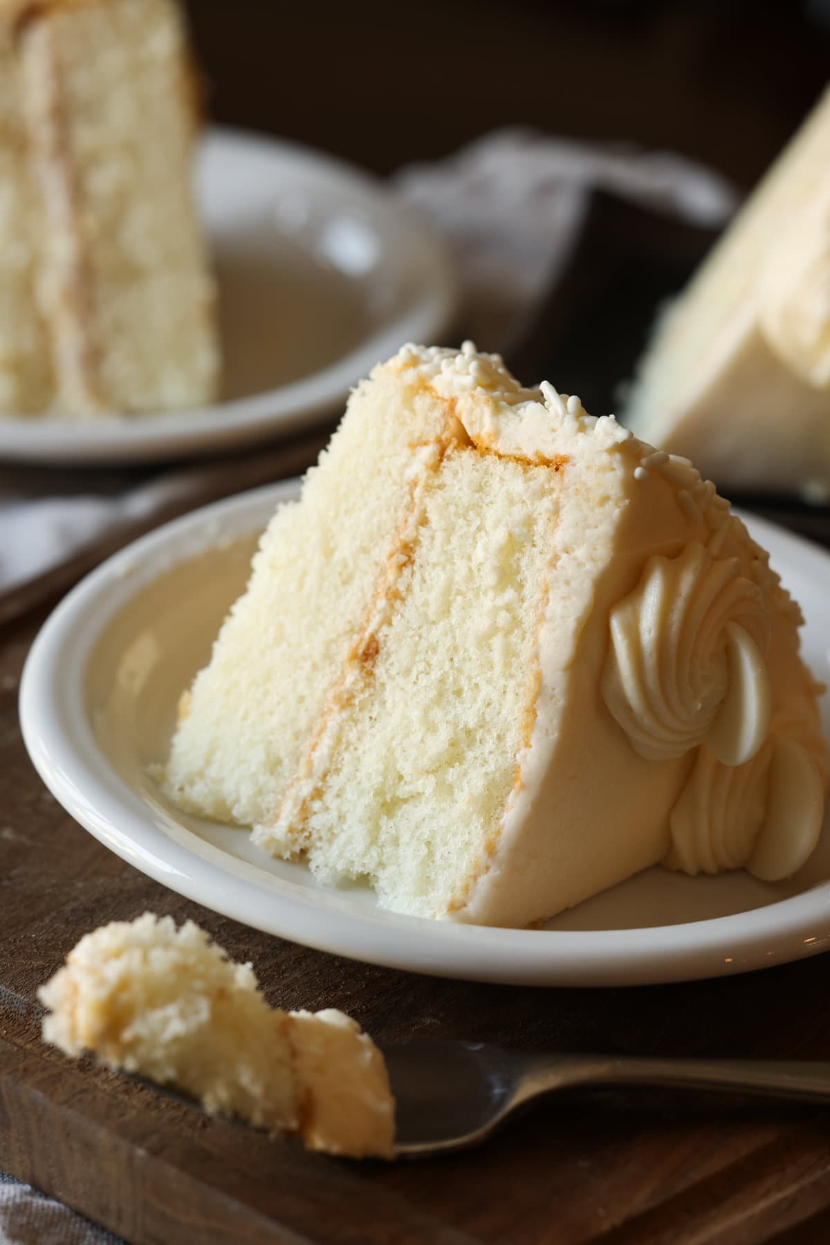 A slice of fluffy white cake made with cake flour on a white plate with buttercream frosting