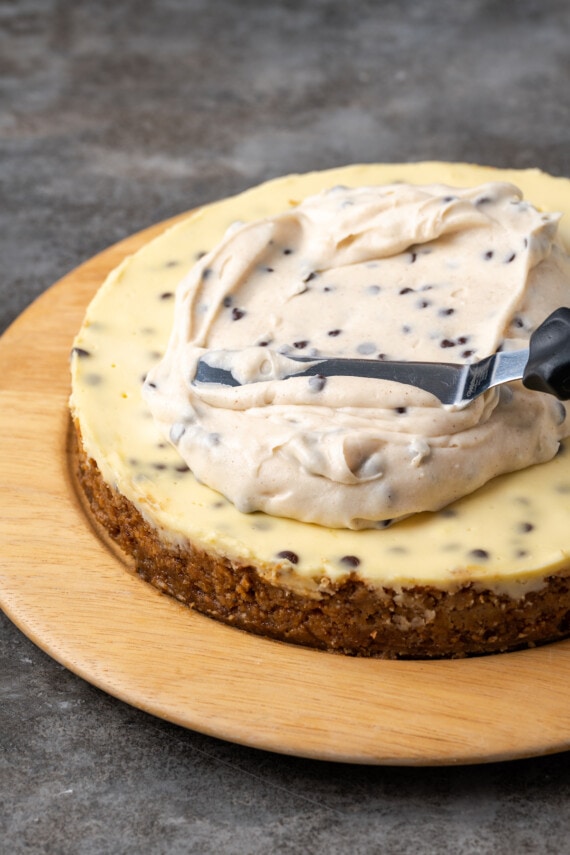 An offset spatula is used to spread cannoli topping over top of the baked cheesecake.