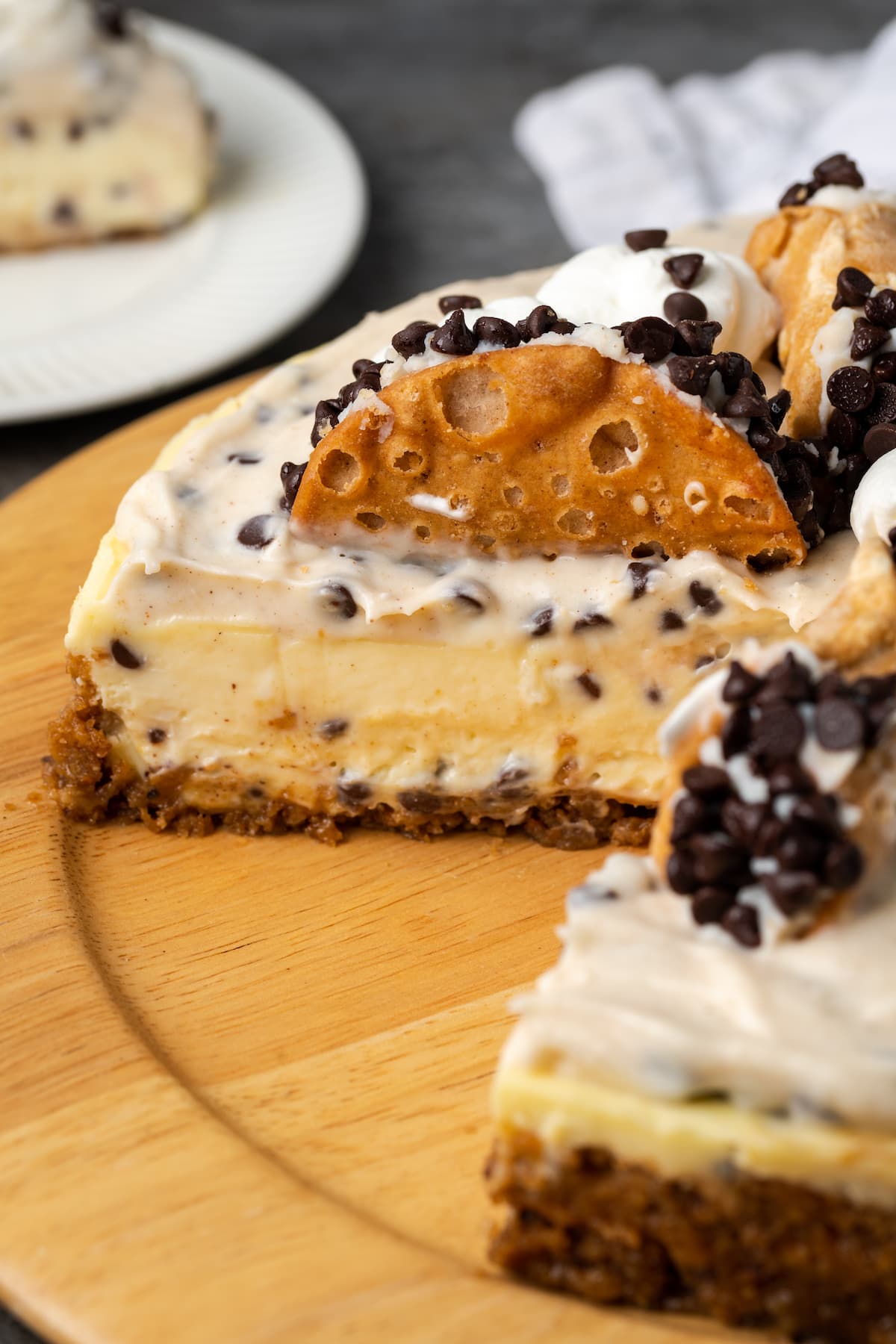 Cannoli cheesecake with a large slice missing on a round wooden platter.