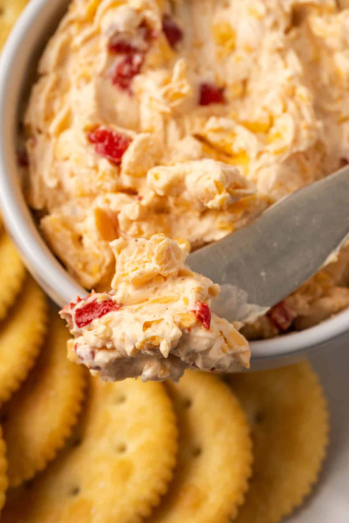 Close up of a bowl of pimento cheese served with a cheese knife on a platter of crackers.