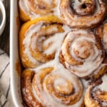 Overhead view of baked TikTok cinnamon rolls covered with icing in a ceramic baking dish.