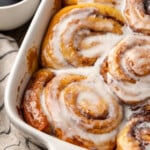 Overhead view of baked TikTok cinnamon rolls covered with icing in a ceramic baking dish, next to a cup of coffee.