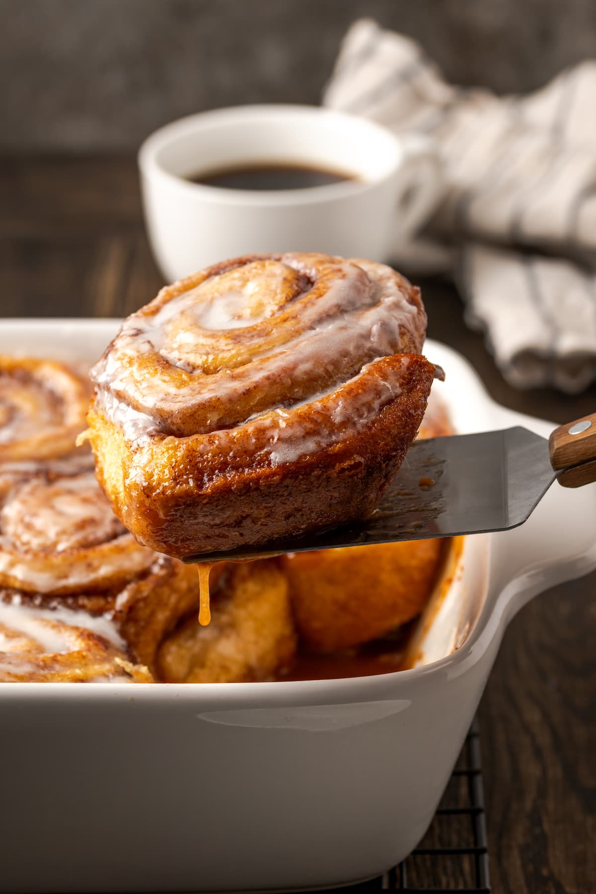 A spatula lifts a TikTok cinnamon roll from a baking dish.