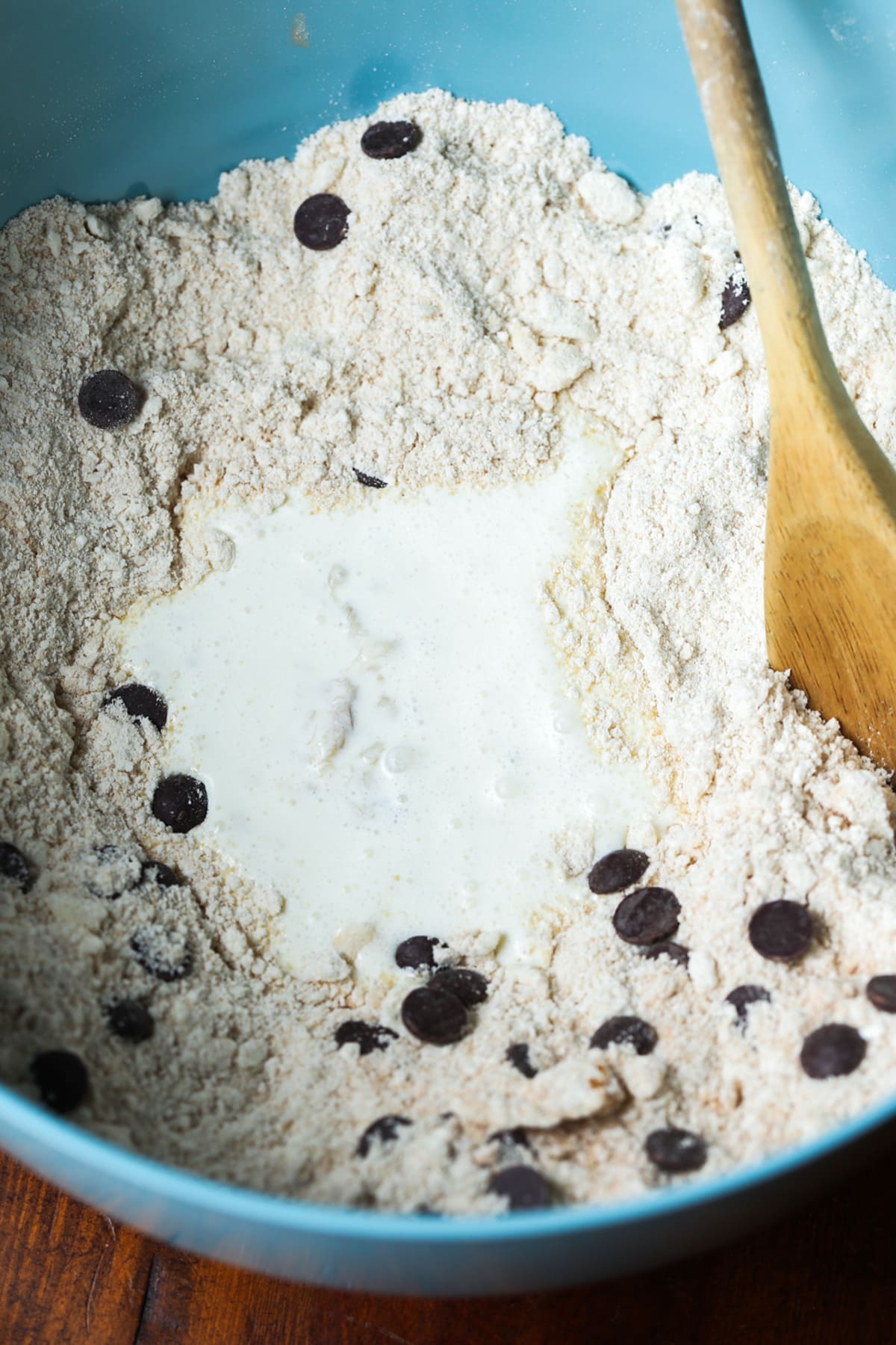 A blue bowl with flour, chocolate chips and heavy cream stirred with a wooden spoon
