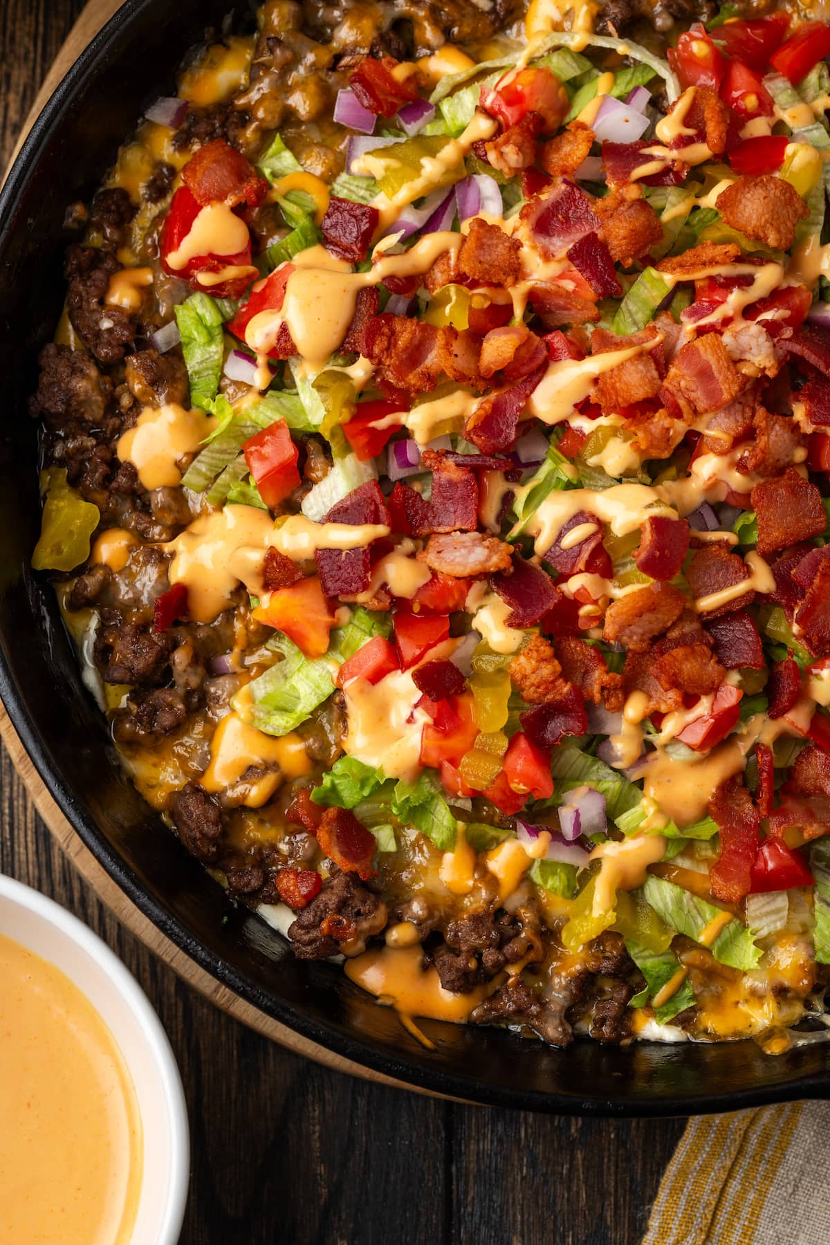 Overhead close up view of a skillet of cheeseburger dip next to a bowl of burger sauce.