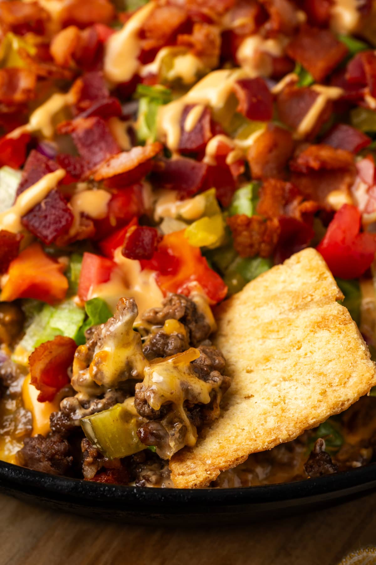 Close up of a pita chip dipped into a skillet of cheeseburger dip.