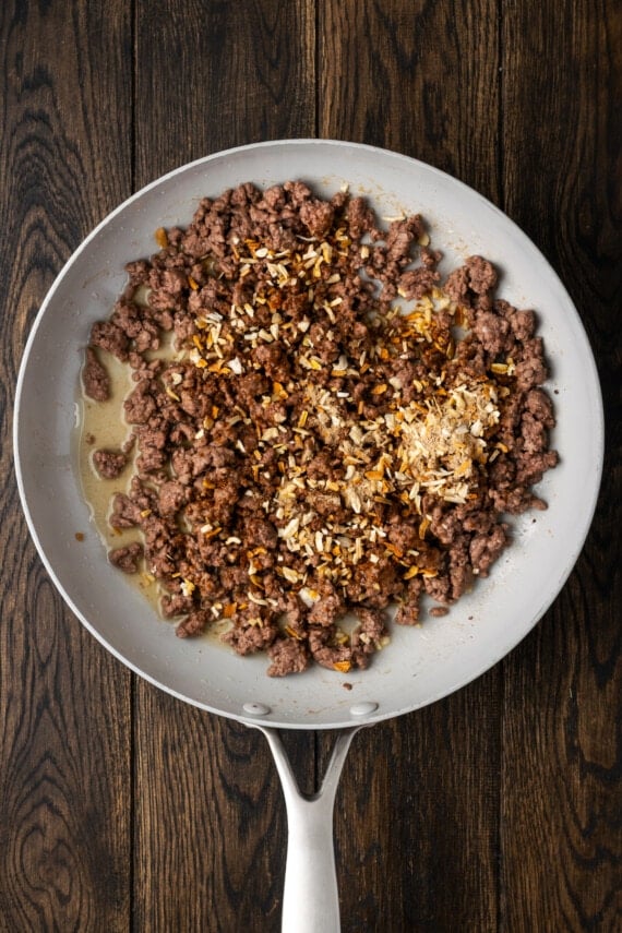 Onion soup mix added to browned ground beef in a skillet.