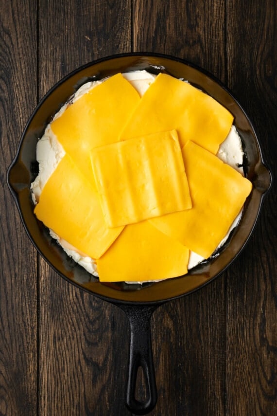 American cheese slices layered over cream cheese and ground beef in cast iron skillet.