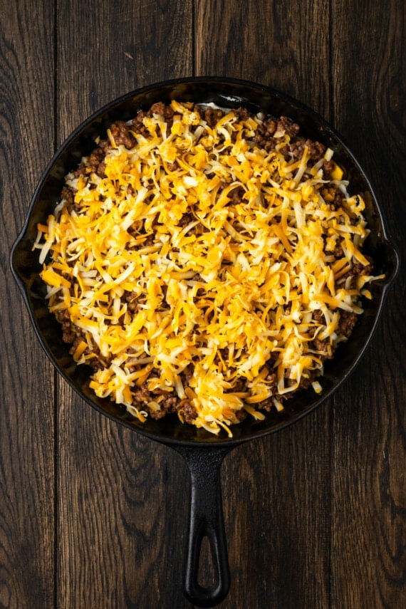 Cheeseburger dip layers topped with shredded cheese in a cast iron skillet.