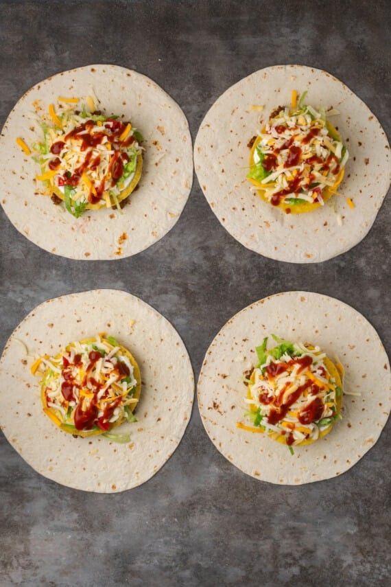 Overhead view of four assembled crunch wraps topped with meat, corn tortillas, veggies, and cheese.