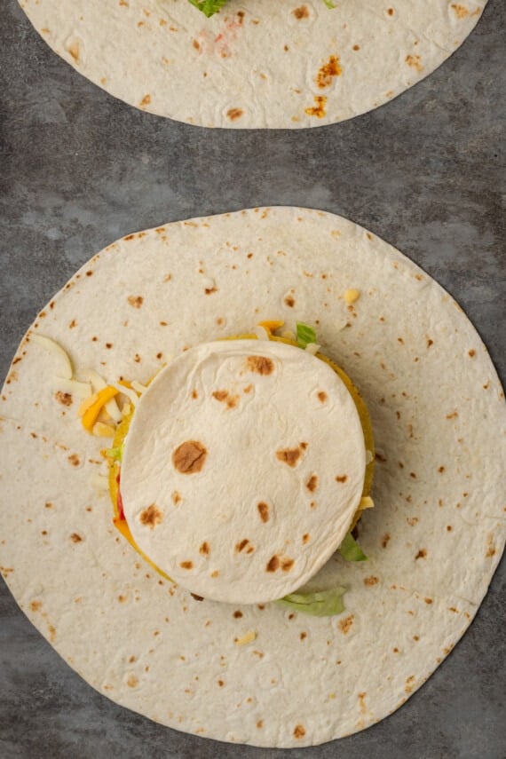A smaller tortilla placed over the fillings of an unfolded crunch wrap.