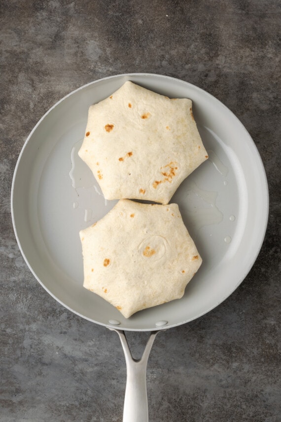 Two folded crunch wraps in a skillet.