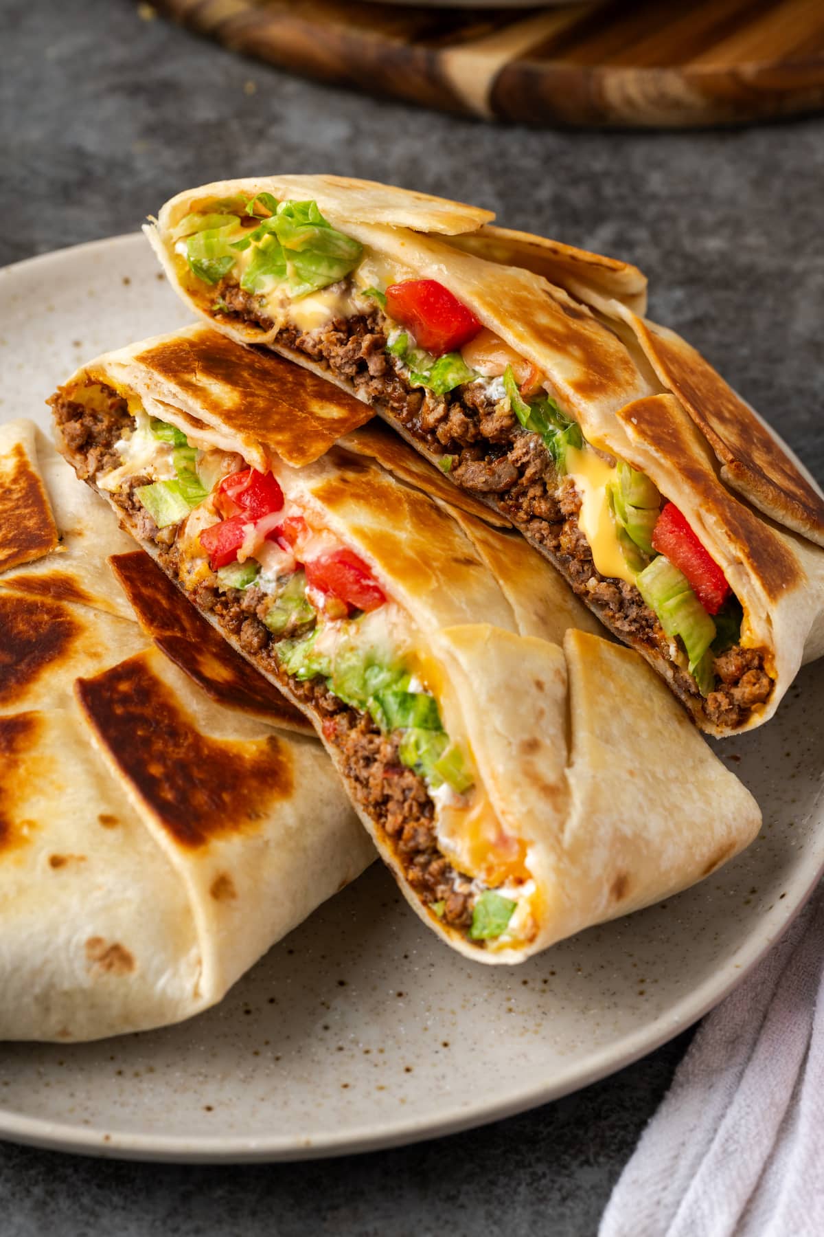 Two pan-fried crunch wraps on a plate, with one crunch wrap cut in half to reveal the layers inside.
