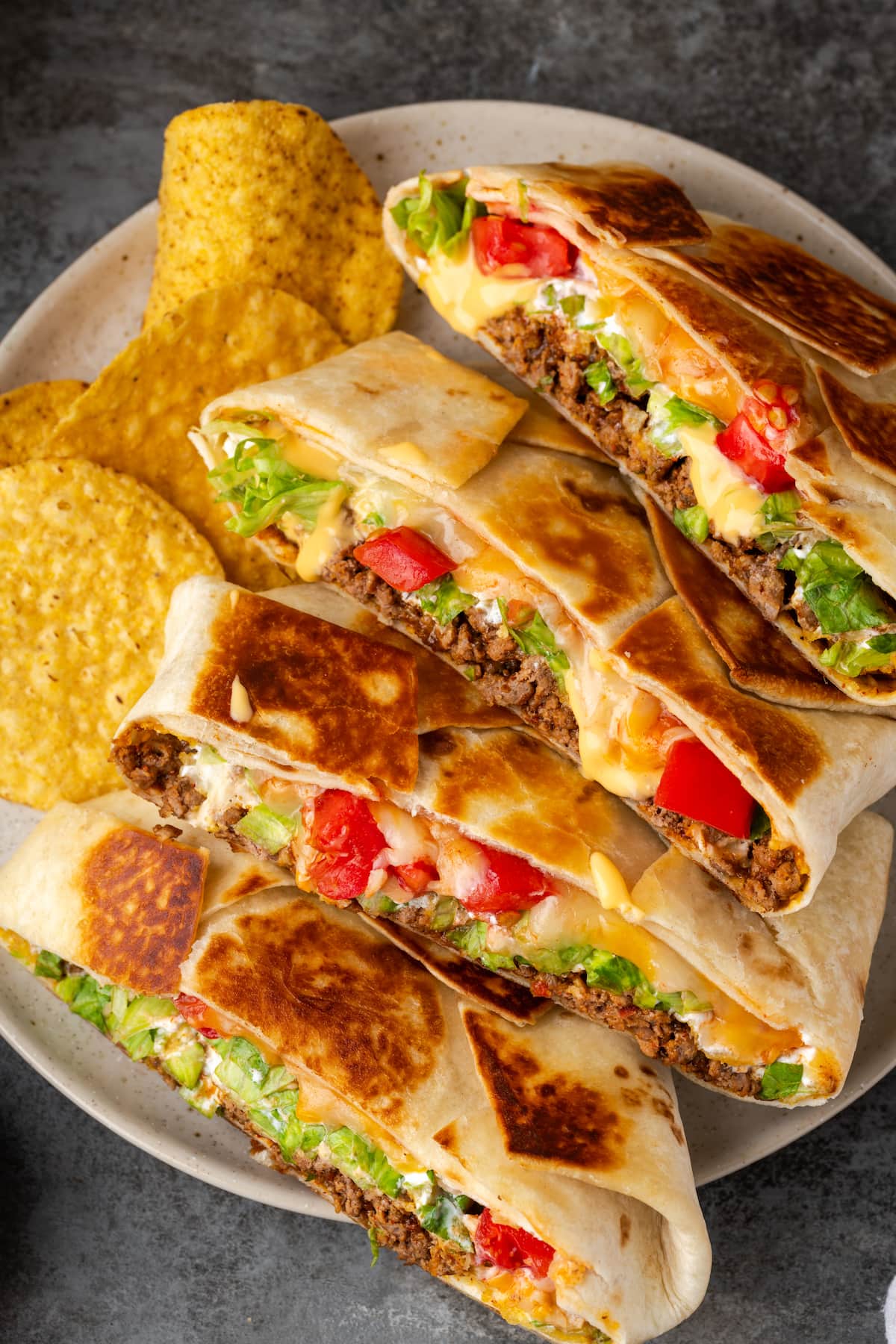 Crunch wraps cut in half and arranged in a row on a plate next to corn chips.