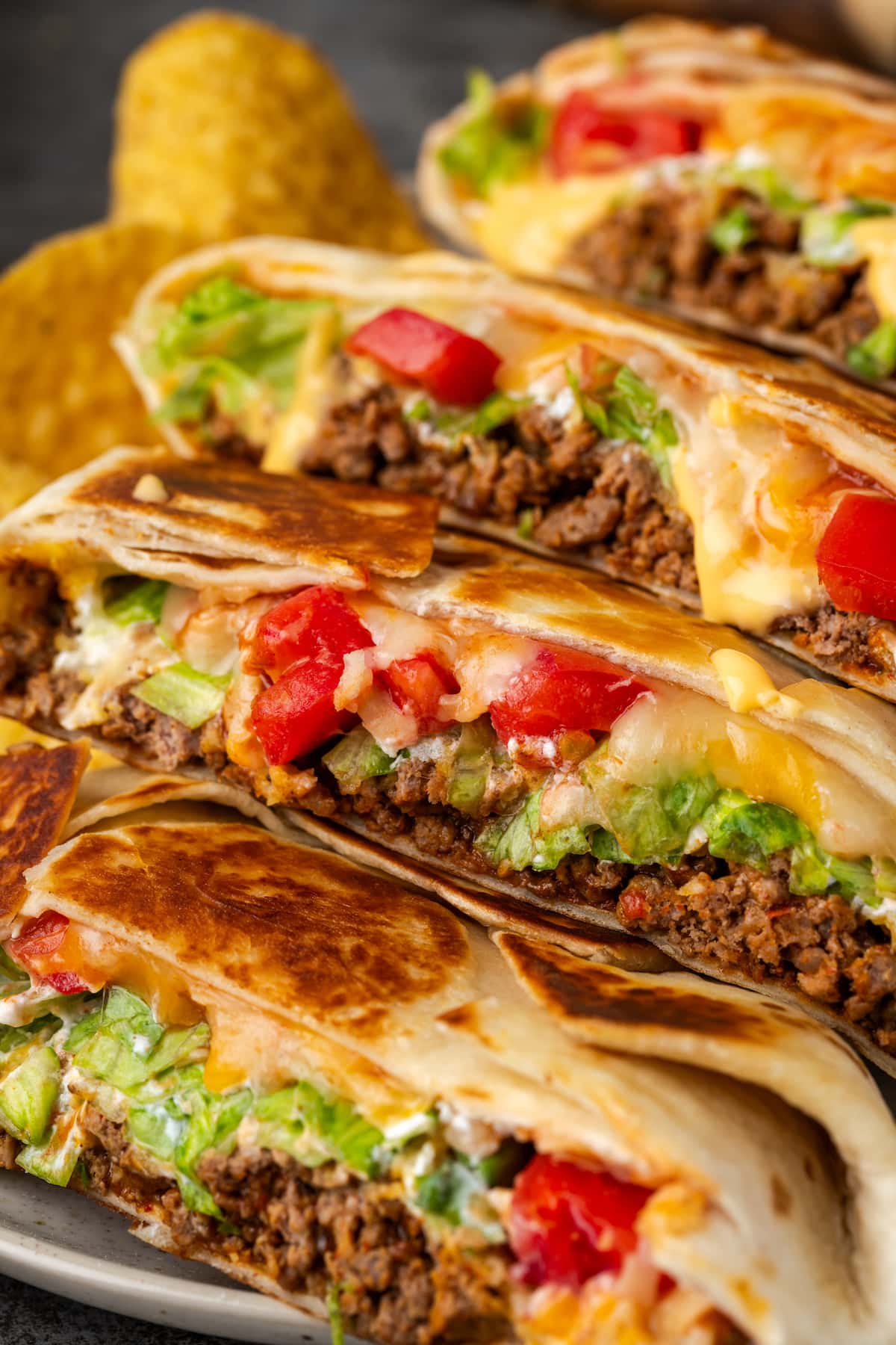 Close up of crunch wraps cut in half and arranged in a row on a plate next to corn chips.