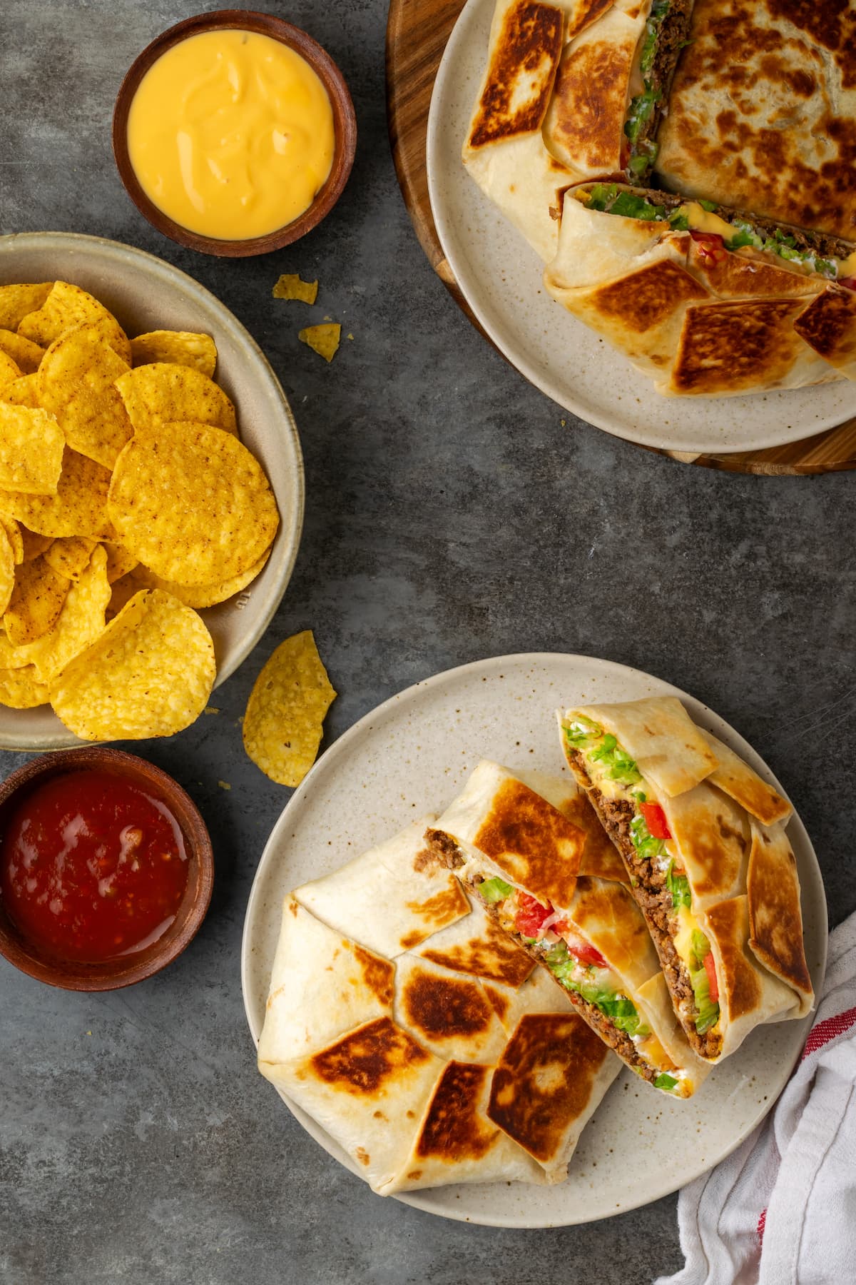Overhead view of crunch wraps served on plates next to a bowl of corn chips and salsa for dipping.