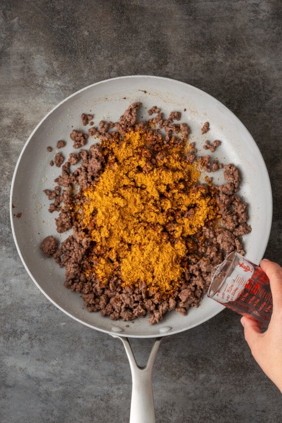 Taco seasoning added to a skillet with browned ground beef.