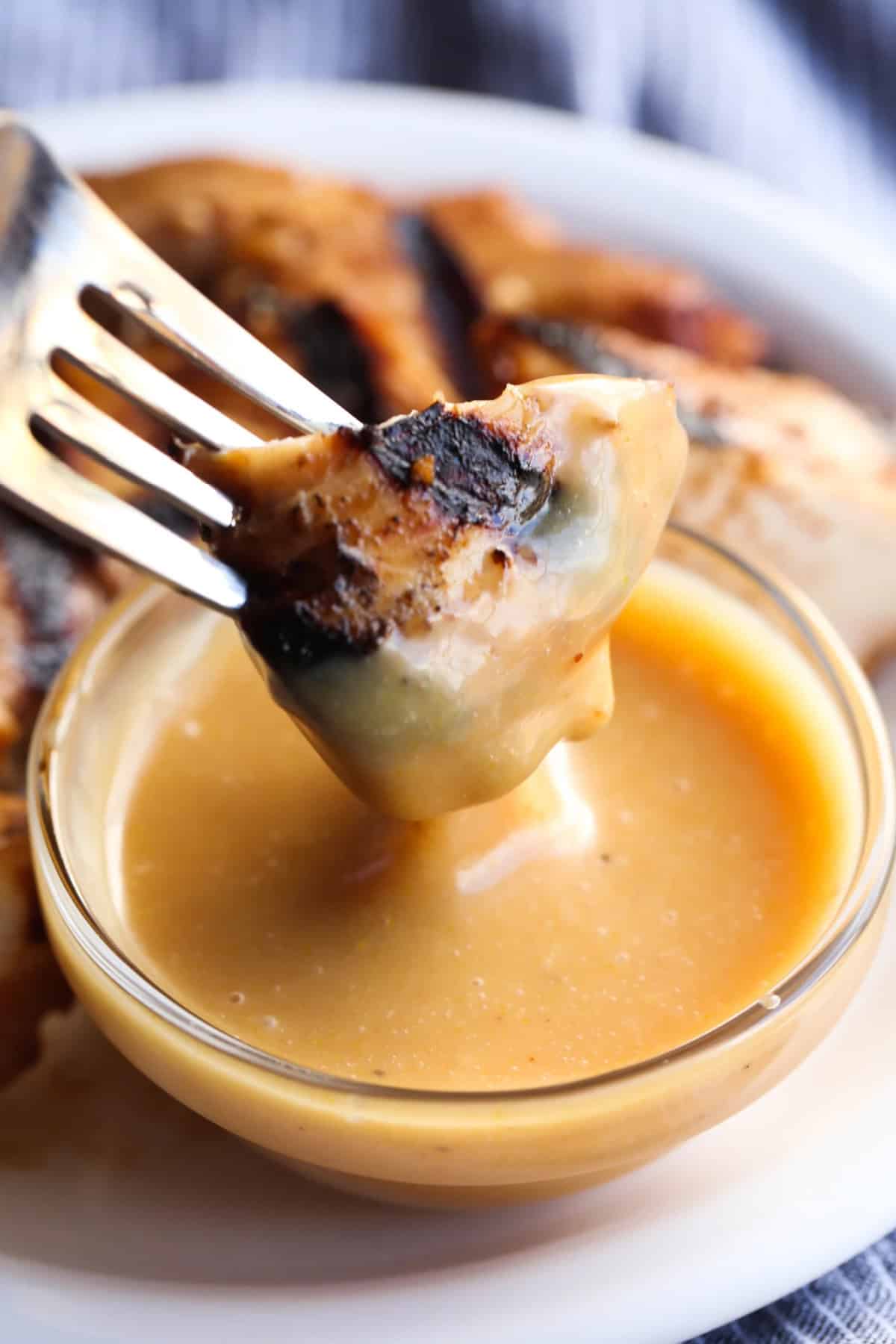 A piece of grilled chicken on a fork coated in homemade chick-fil-a chicken sauce