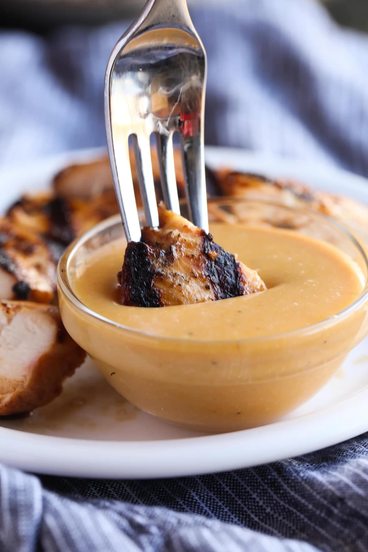 Dunking a piece of grilled chicken into a small bowl of homemade Chick-Fil-A Sauce using a fork