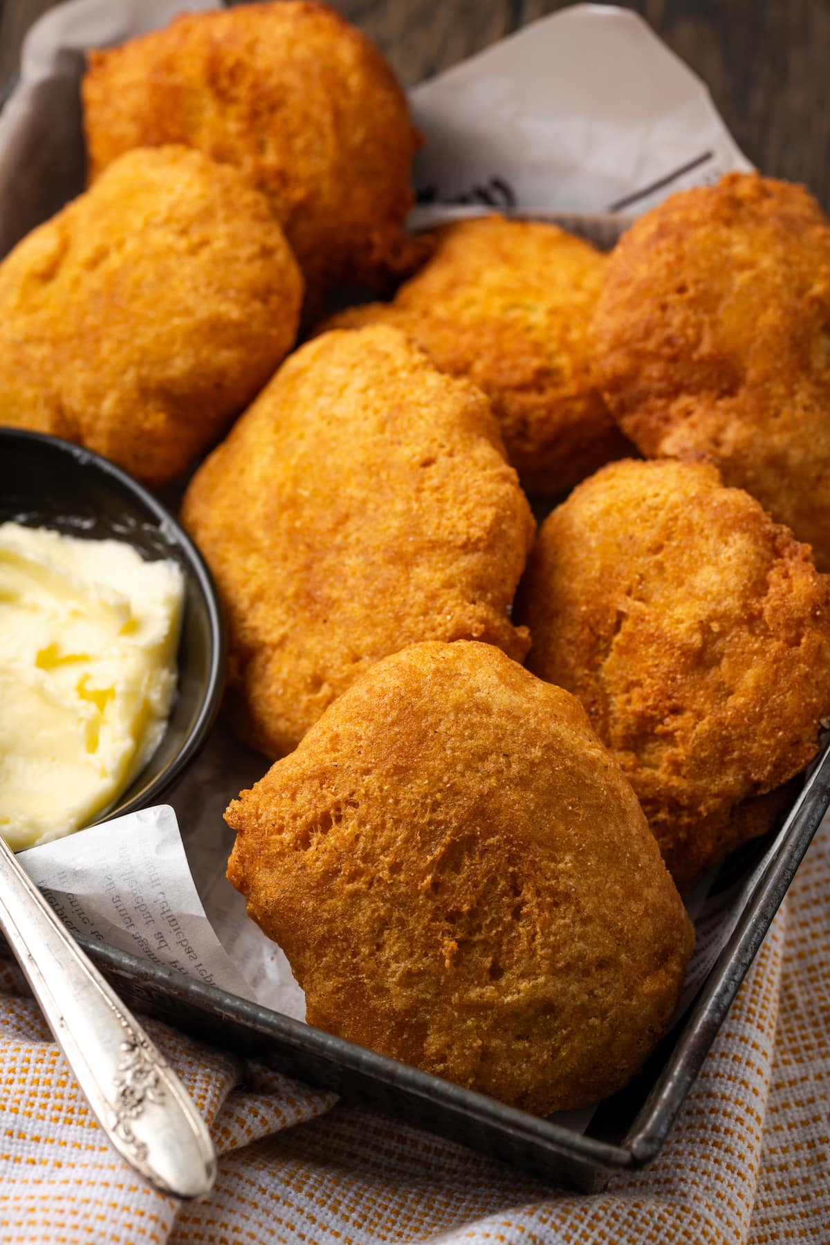 Close up of hot water cornbread served in a basket next to a small dish of butter, with a knife for spreading.