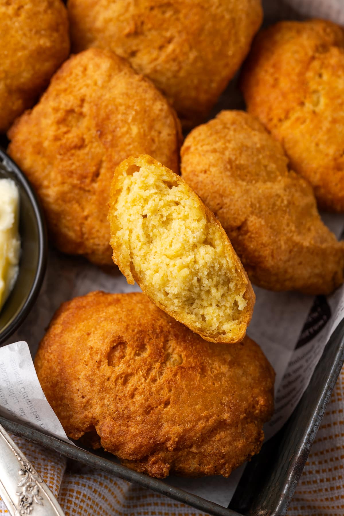 Close up of hot water cornbread in a basket, with one fritter broken in half.