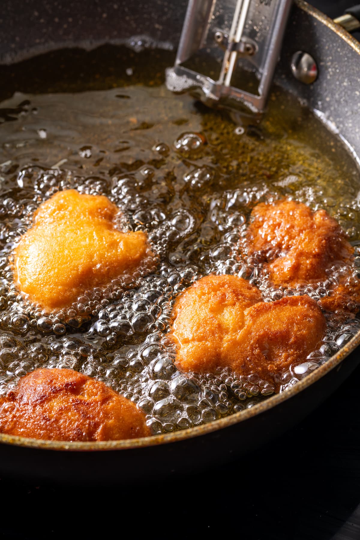 Hot water cornbread fritters deep-frying in a skillet.