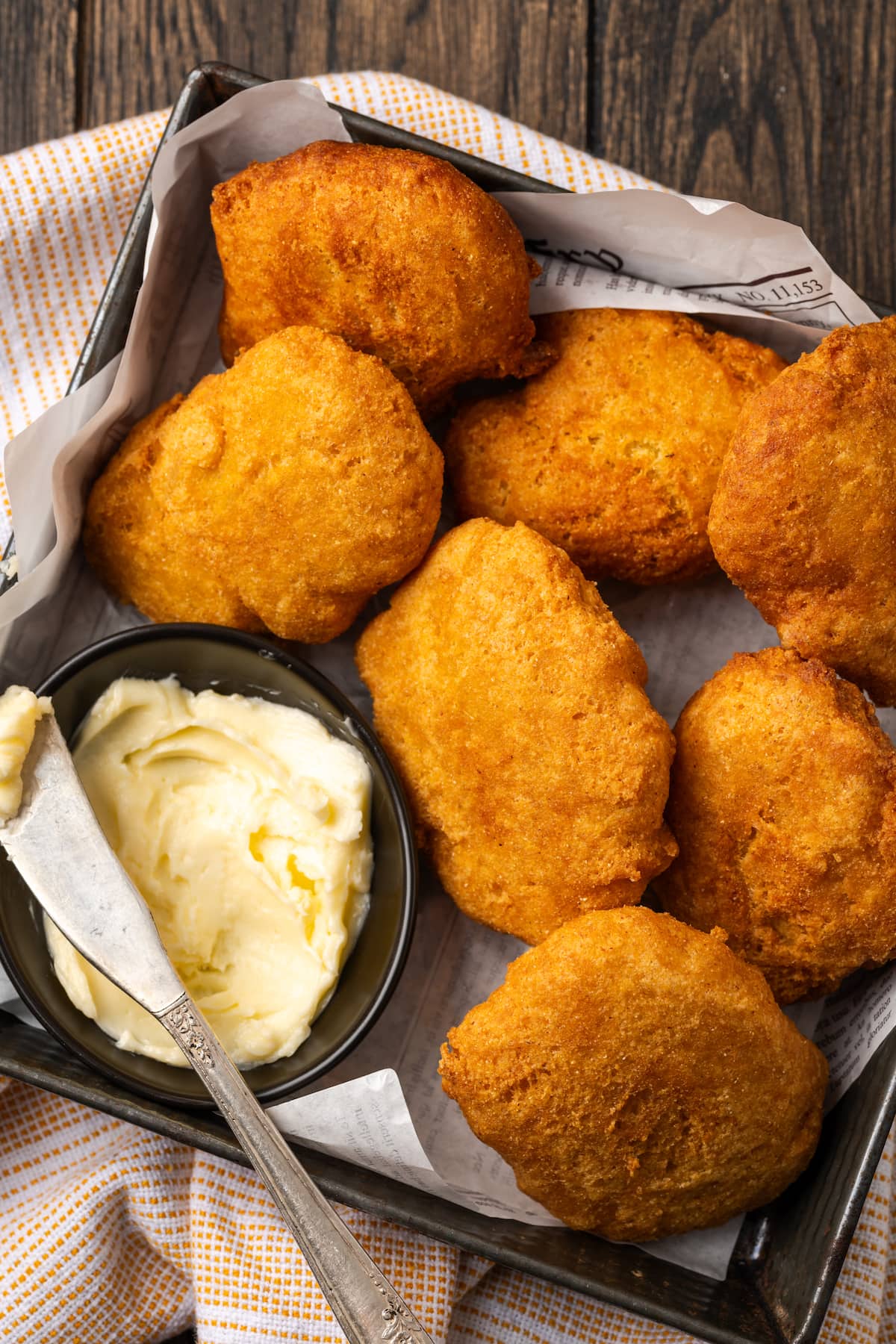 Overhead view of hot water cornbread served in a basket next to a small dish of butter, with a knife for spreading.