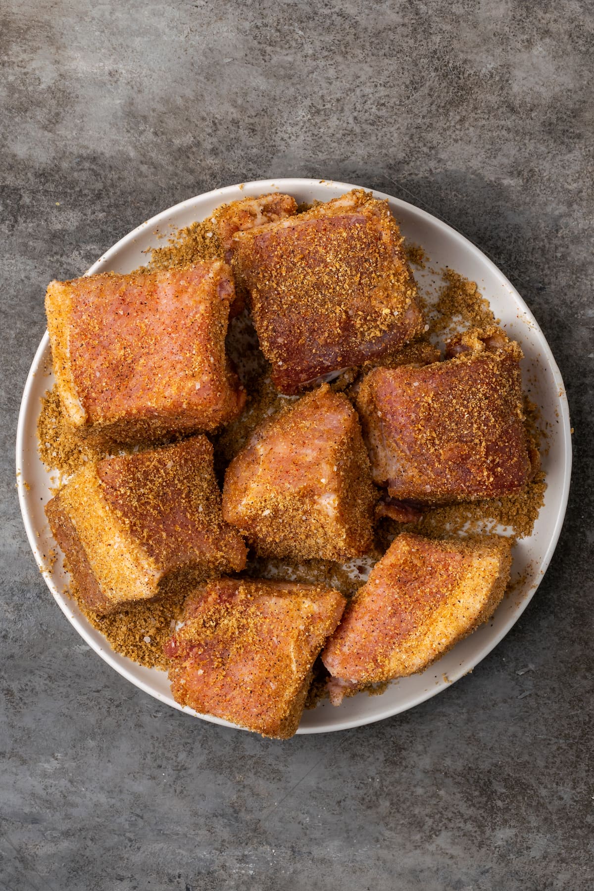Pieces of pork butt coated in seasoning rub on a plate.