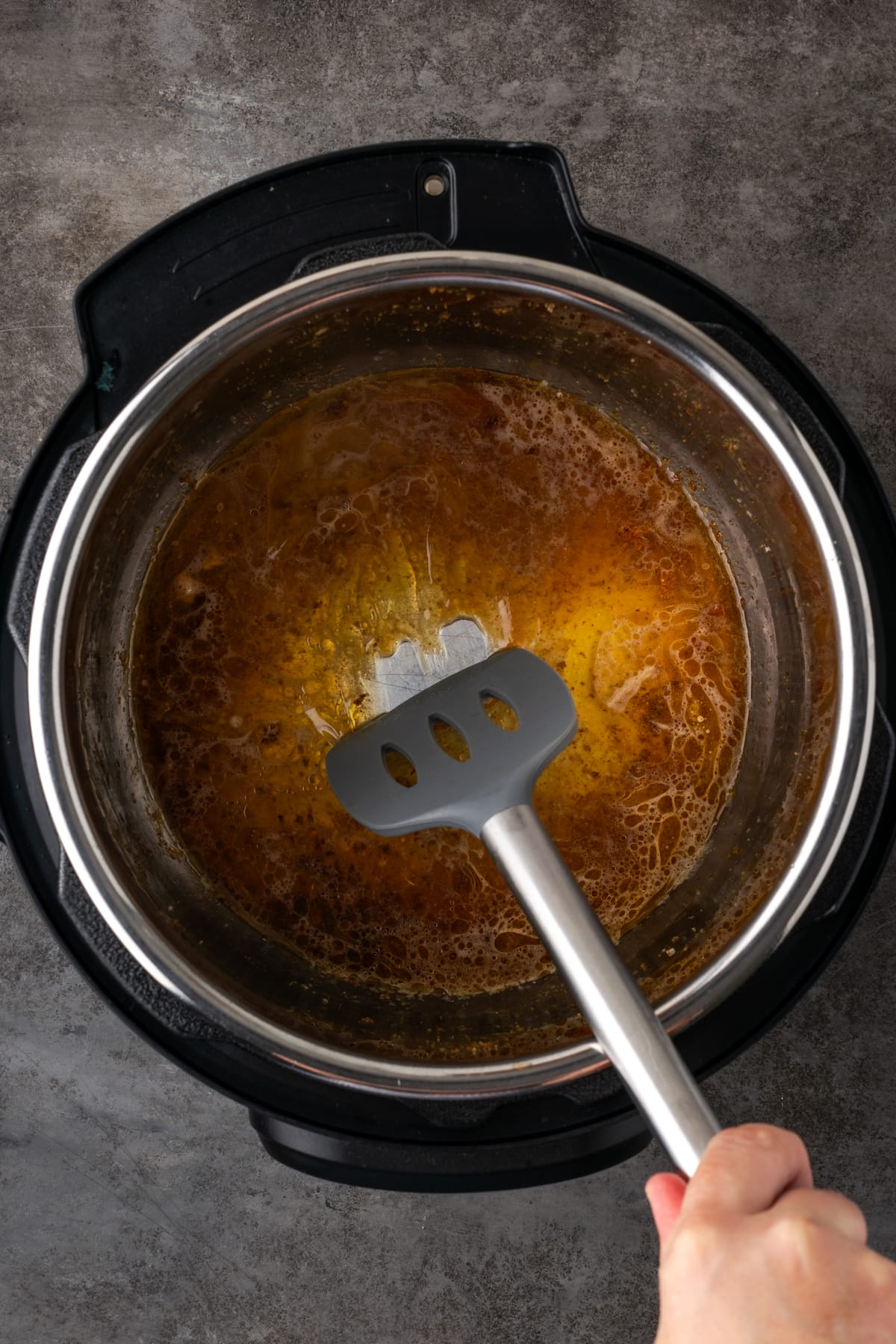 A spatula is used to deglaze the bottom of the instant pot.