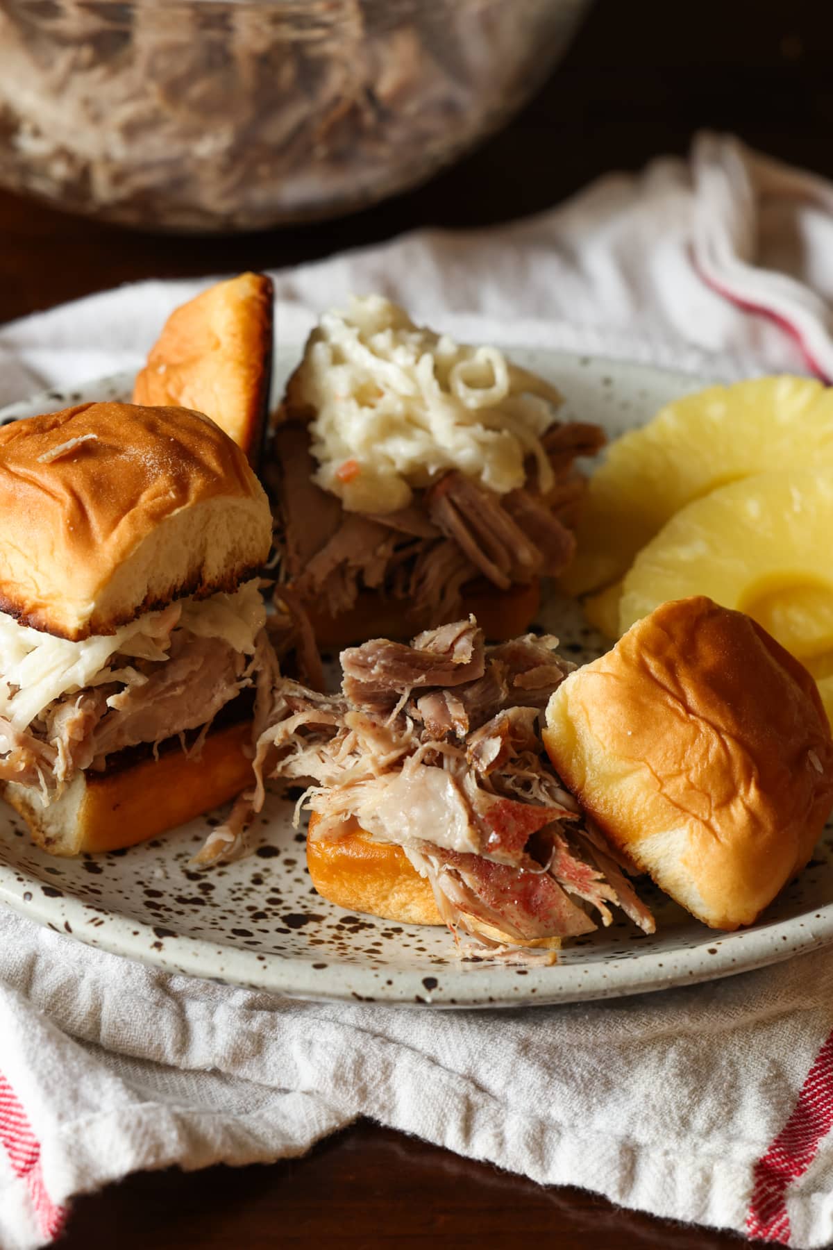 Pulled pork on a Hawaiian roll on a plate with pineapple slices