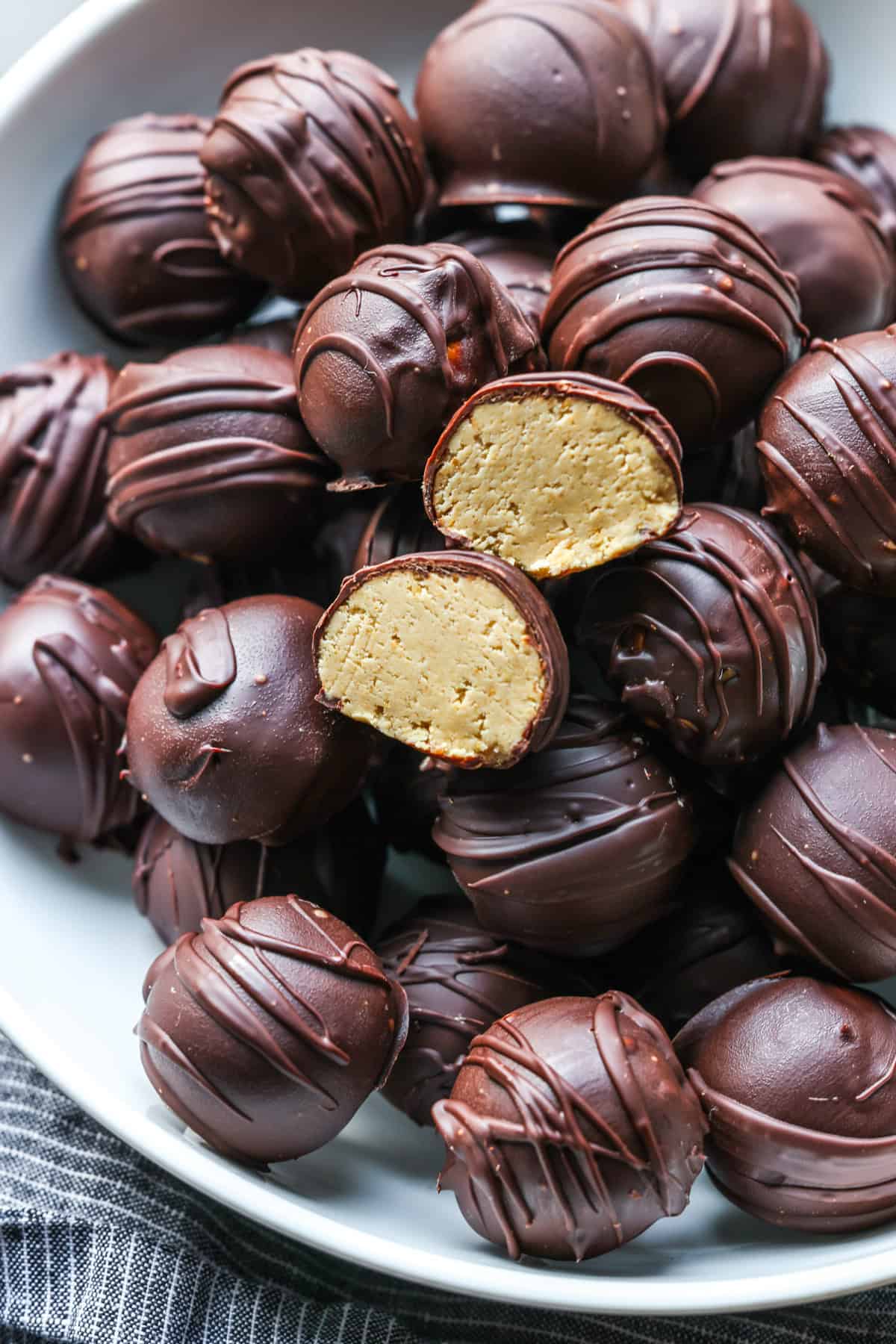 Peanut Butter balls in a white serving bowl with one cut in half showing the inside.