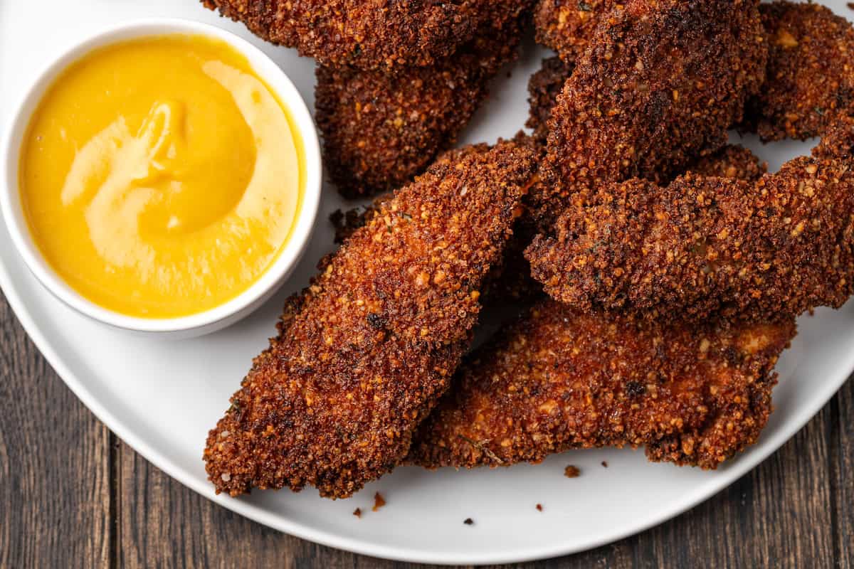 Overhead view of pecan crusted chicken tenders on a plate next to a bowl of dipping sauce.