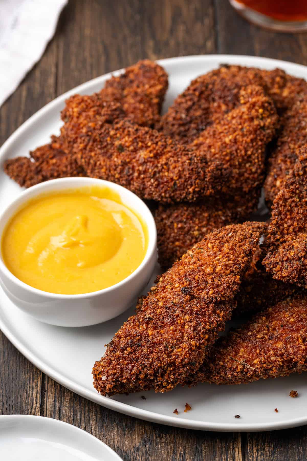 Pecan crusted chicken tenders on a plate next to a bowl of dipping sauce.