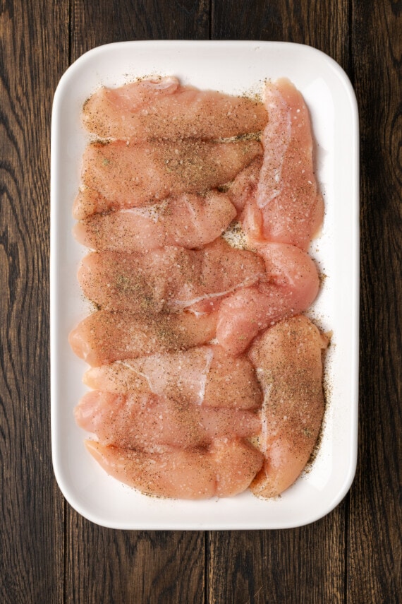 Chicken strips seasoned with salt and pepper on a plate.