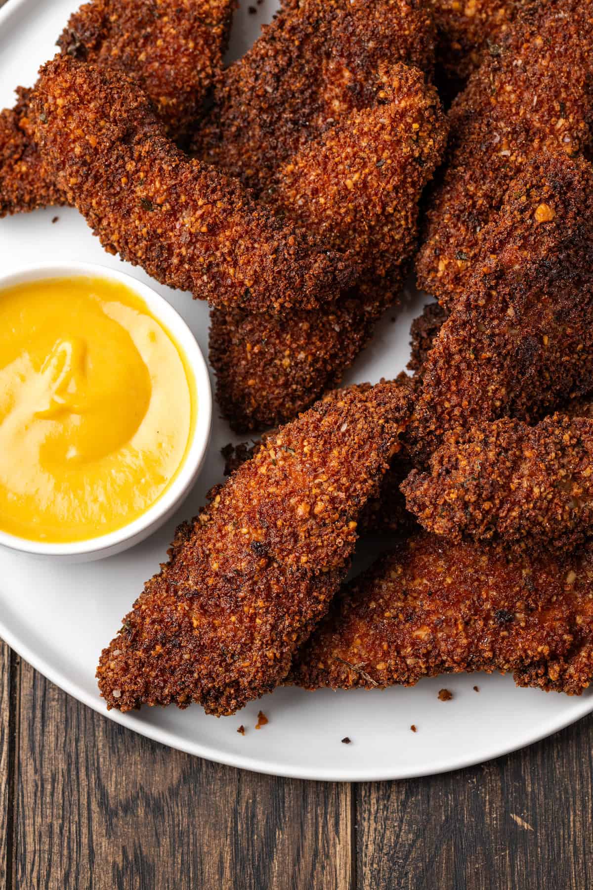 Overhead view of pecan crusted chicken tenders on a plate next to a bowl of dipping sauce.