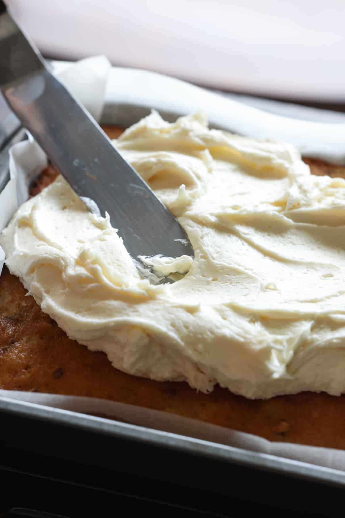 Spreading cream cheese icing onto a cake with an offset spatula