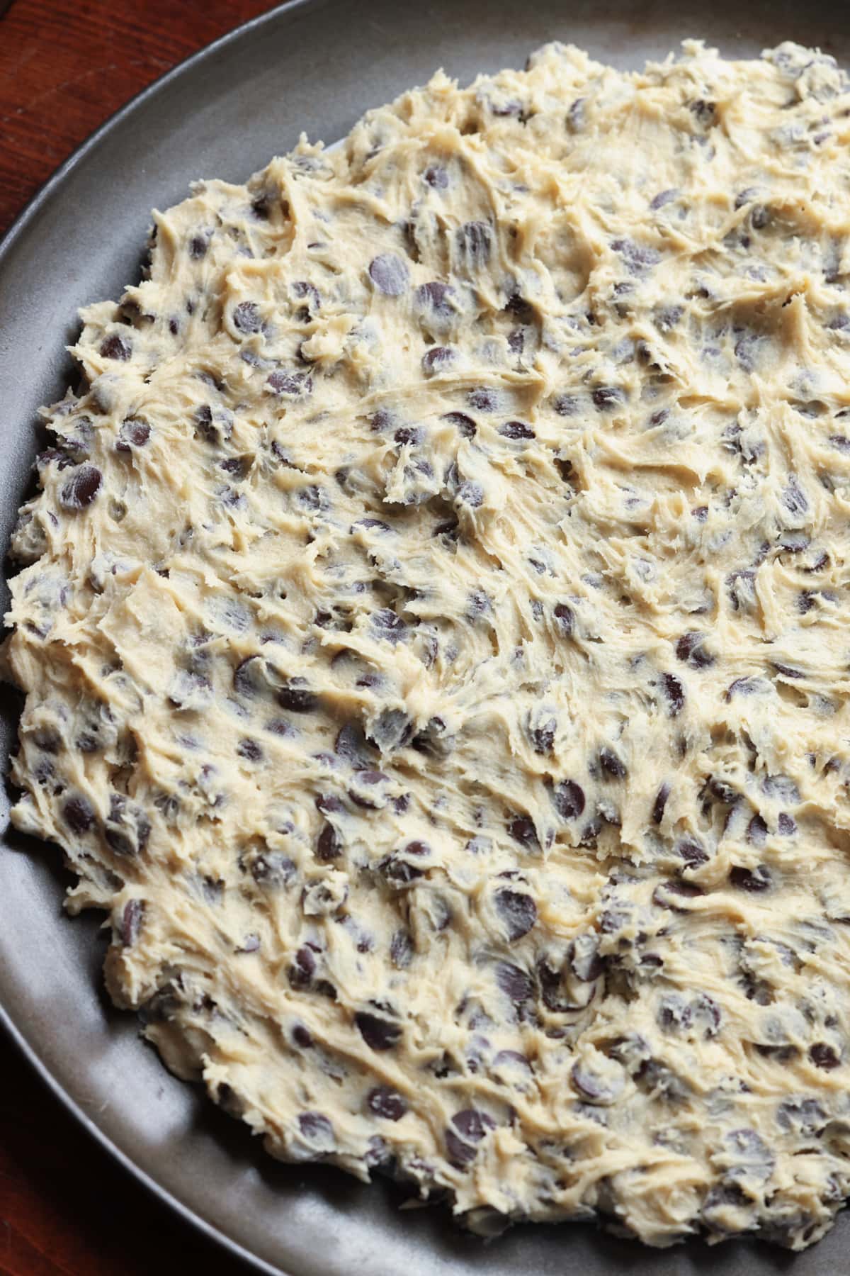 Chocolate chip cookie dough pressed into a nonstick round pizza pan before going in the oven.