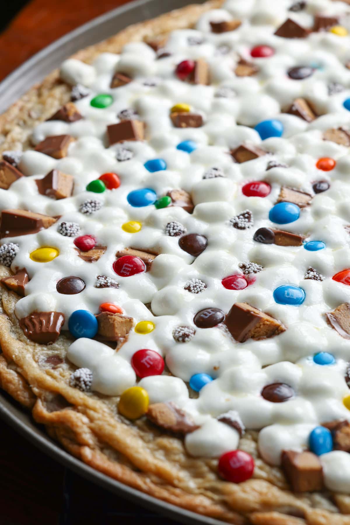 A close up of a large cookie pizza topped with chocolate candy and marshmallows