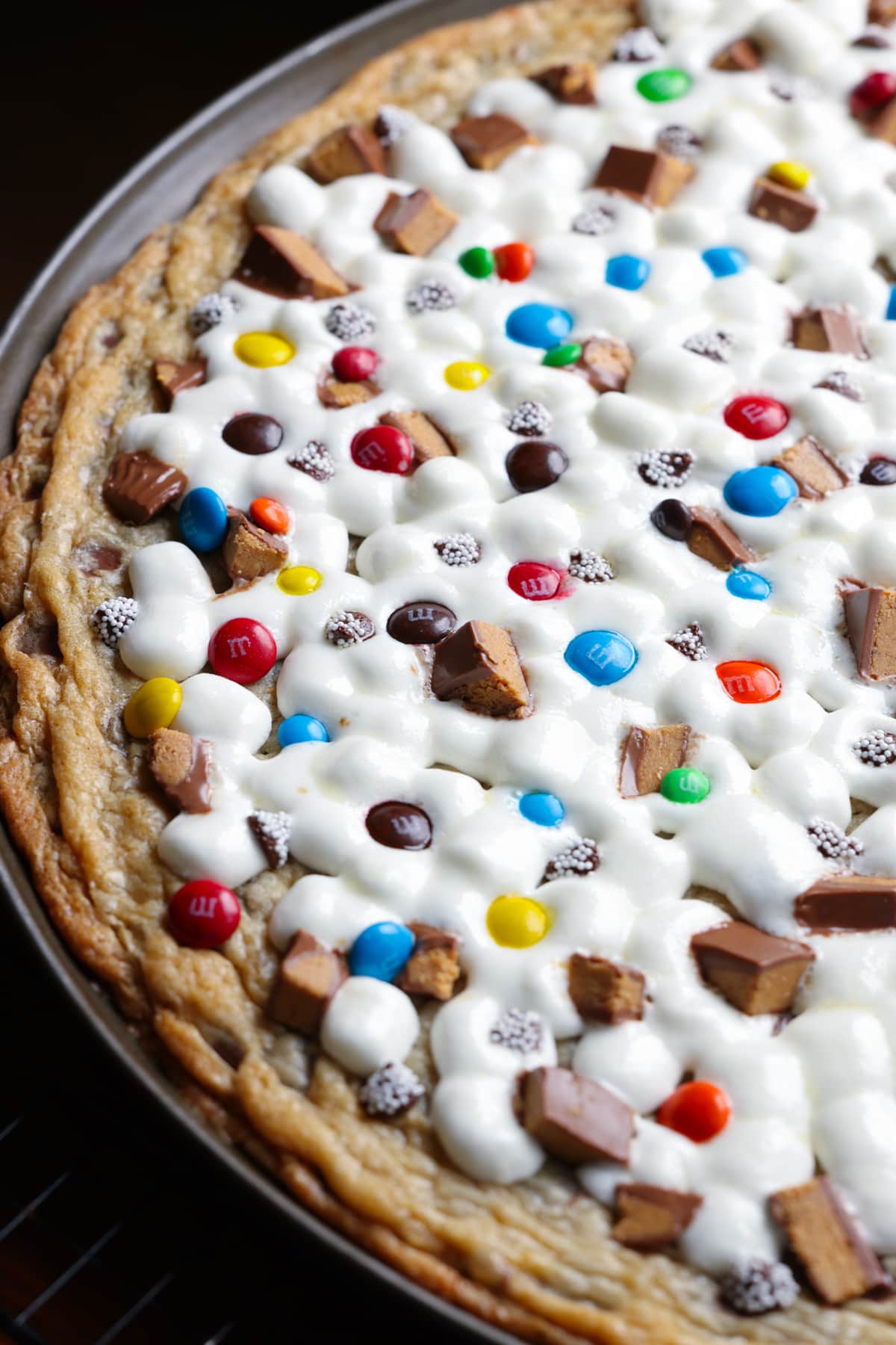 A giant chocolate chip cookie baked in a pizza pan topped with gooey melted marshmallows