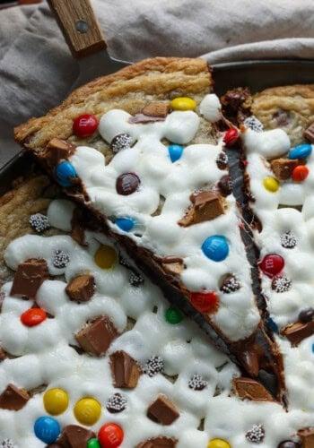 A slice of chocolate chip cookie pizza topped with melted marshmallows, M&Ms, and chopped peanut butter cups