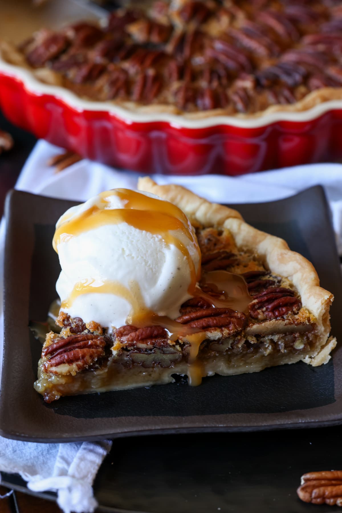 A slice of pecan tart with a scoop of vanilla ice cream and caramel sauce