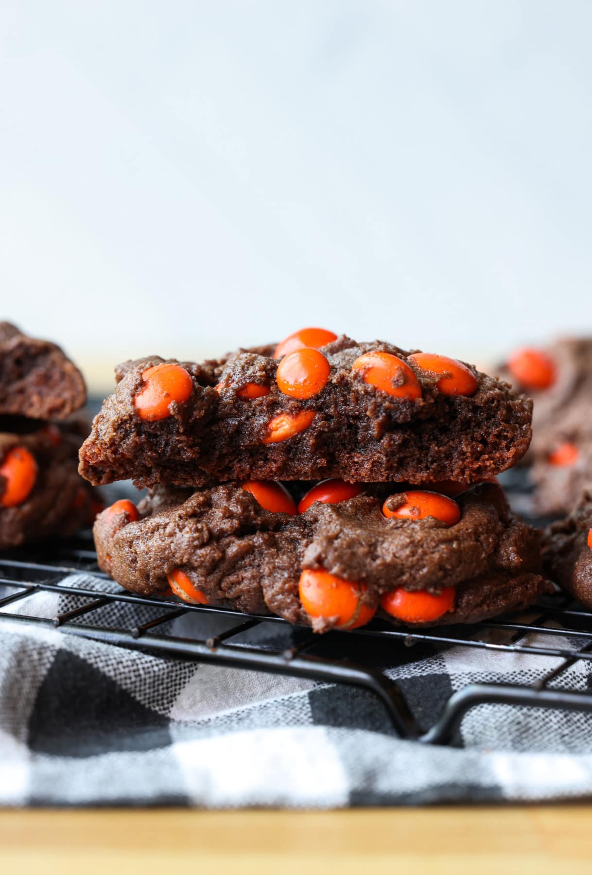 Two chocolate cookies with M&Ms stacked and the top one broken in half showing the fudgy interior