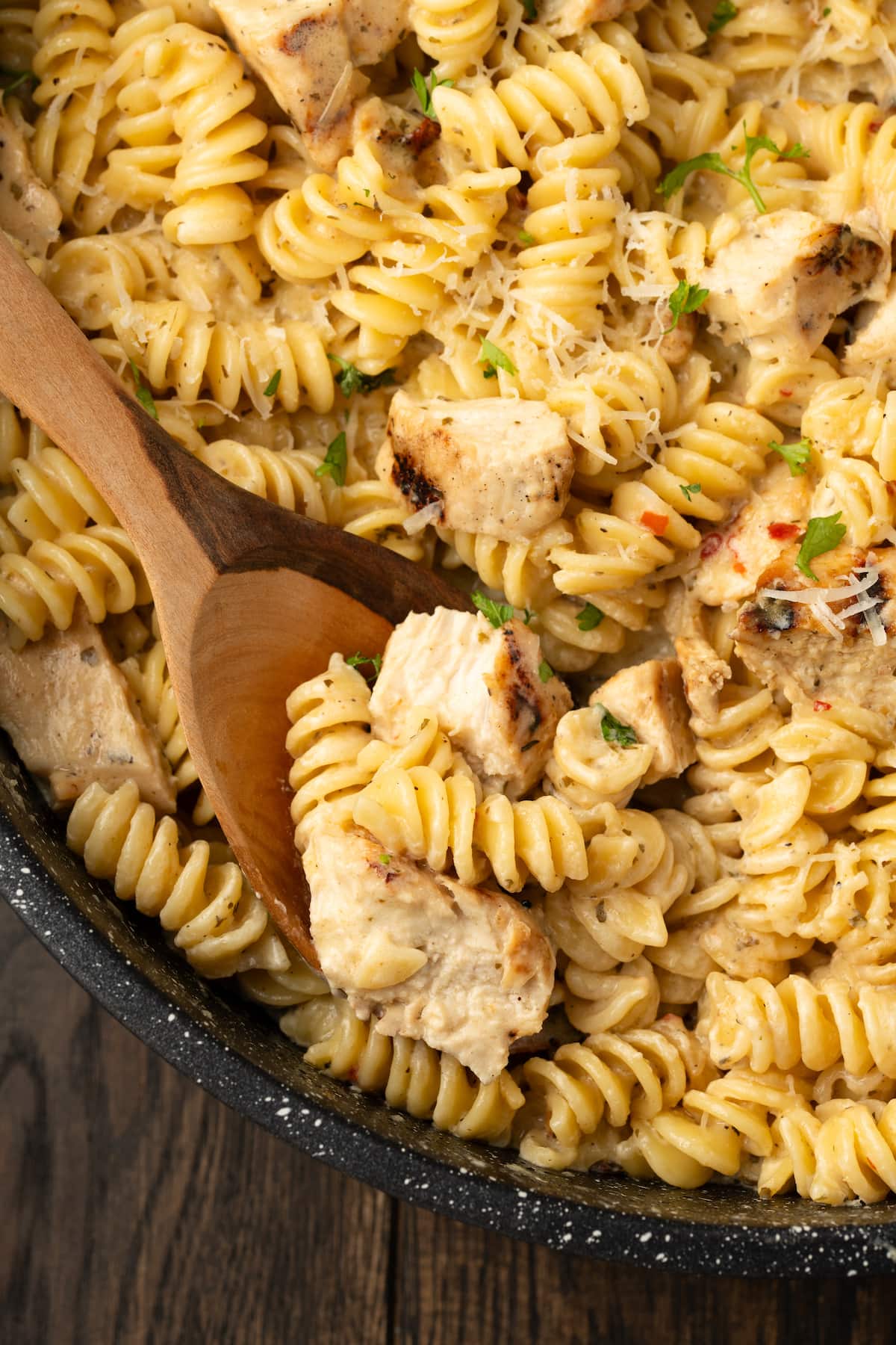 Close up of Buffalo Wild Wings garlic parmesan chicken pasta in a skillet with a wooden spoon.