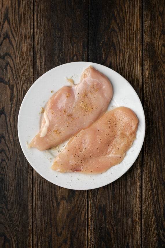 Two uncooked, seasoned chicken breasts on a white plate.