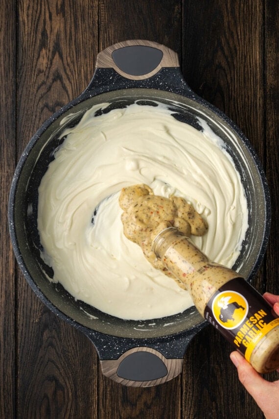 Buffalo wing sauce added to a skillet with melted cream cheese.