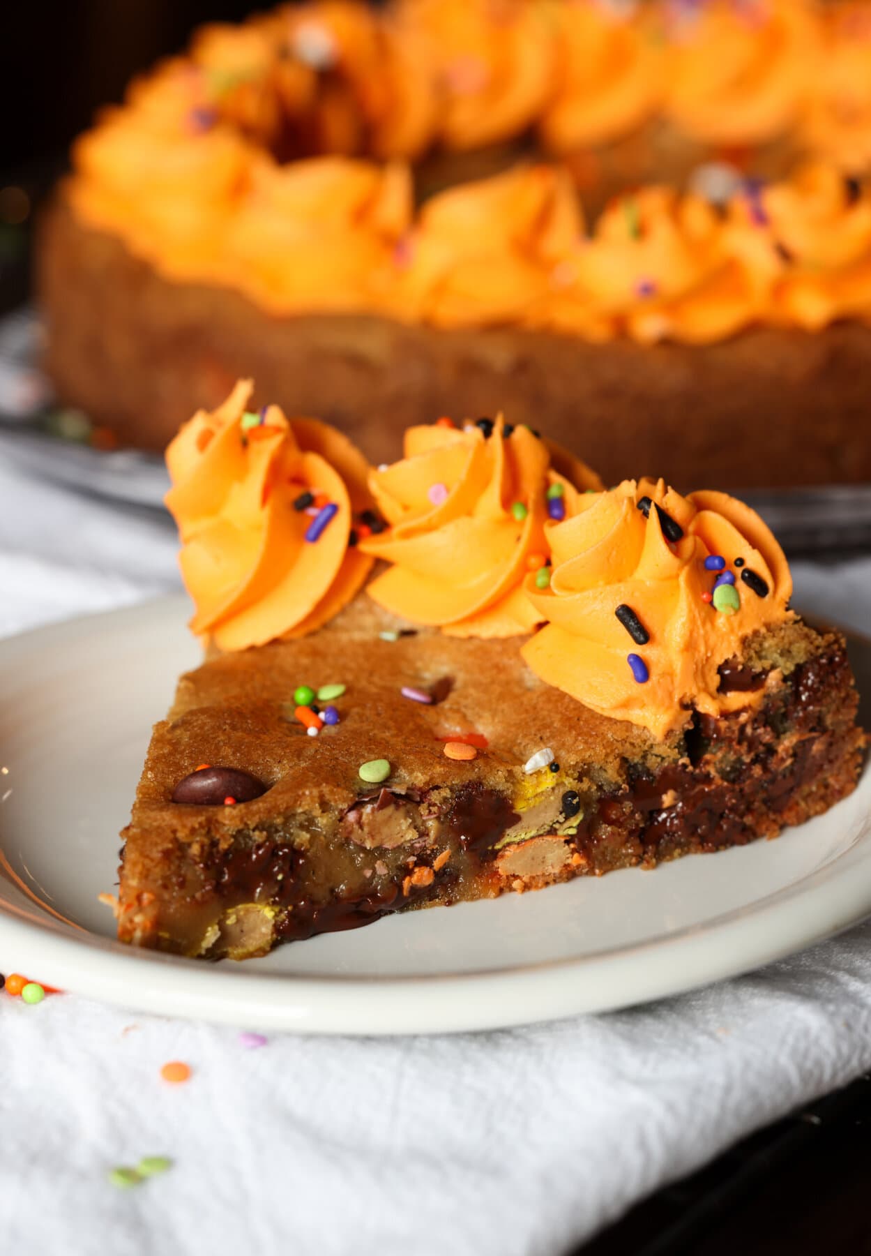 A slice of cookie cake on a white plate with orange frosting